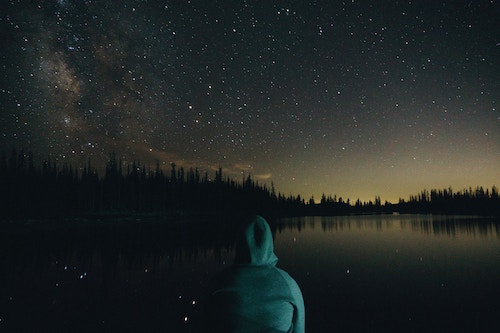 Photo of person looking over a lake on a starry night